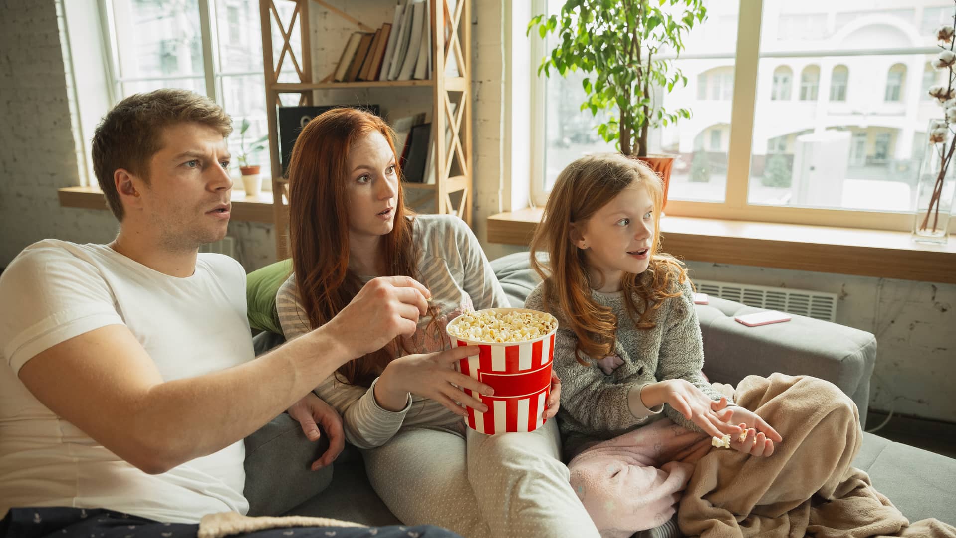 Familia come palomitas mientras ve con interés una película de disney plus en su smart tv Familia come palomitas mientras ve con interés una película de disney plus en su smart tv
